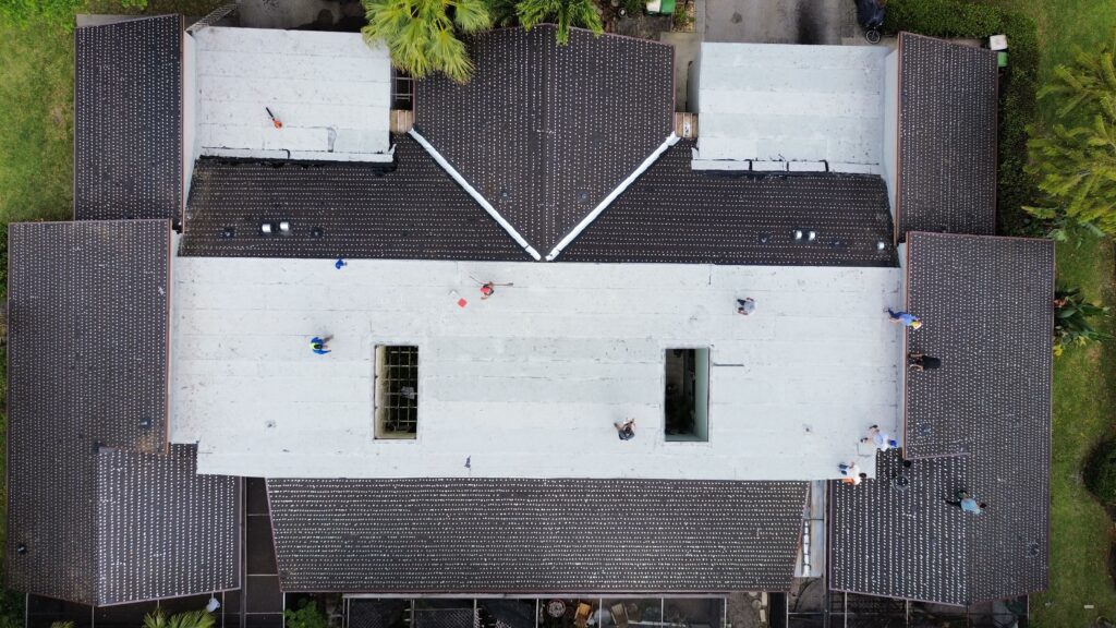 Overhead view of a building with a white flat roof and dark shingle sections