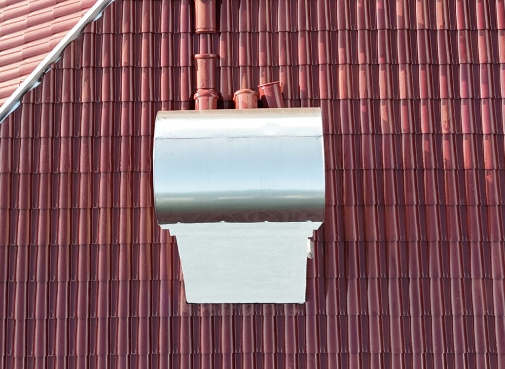 Metal chimney cap on a red tile roof