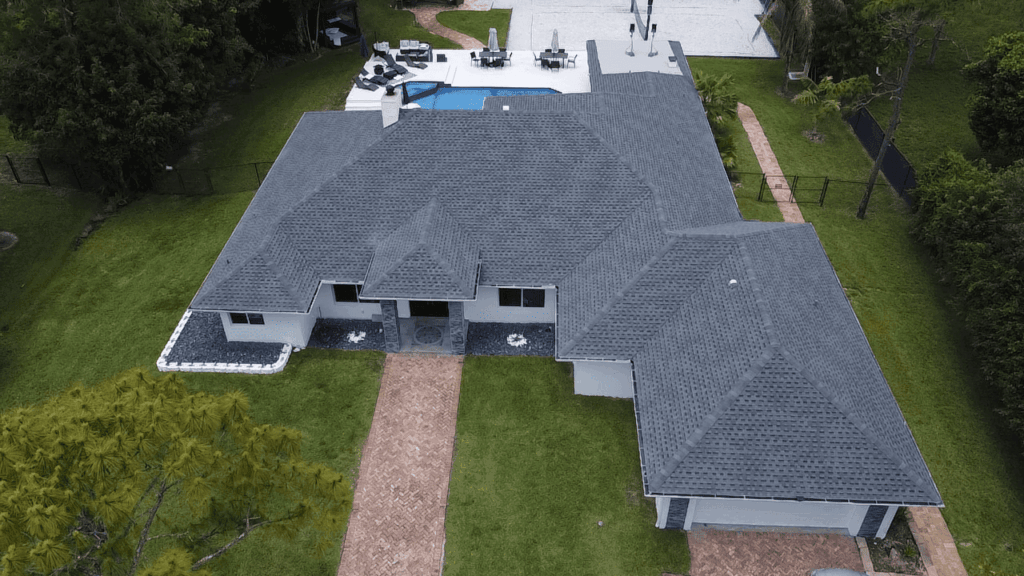 Aerial view of a large home with a dark gray shingle roof and long driveway