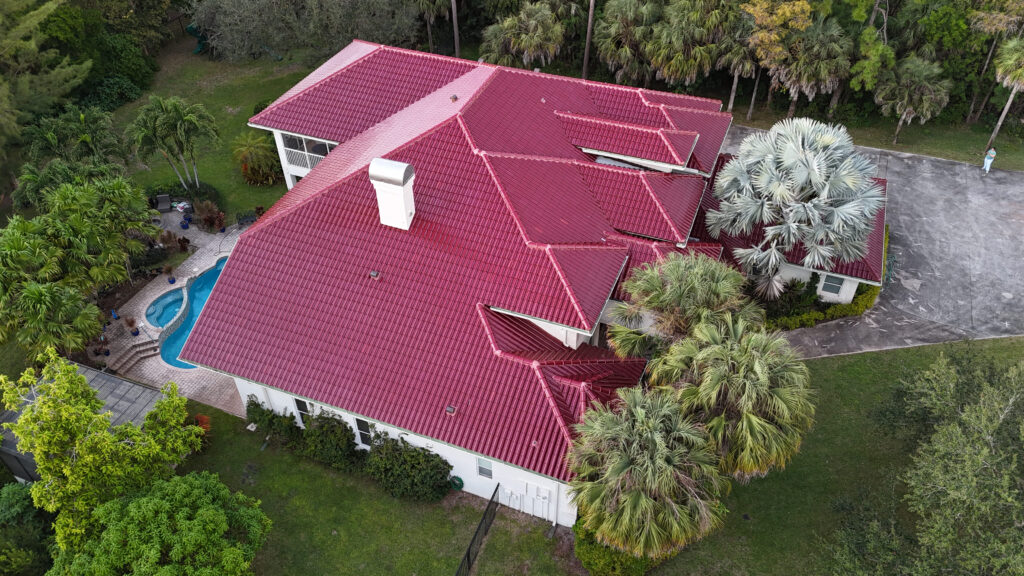 Aerial view of a home with a red metal roof, a pool and tropical landscaping
