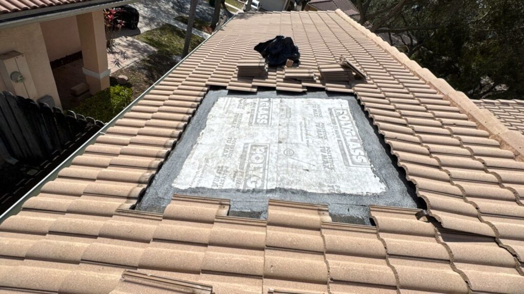 Tile roof under repair with the damaged section stripped to underlayment